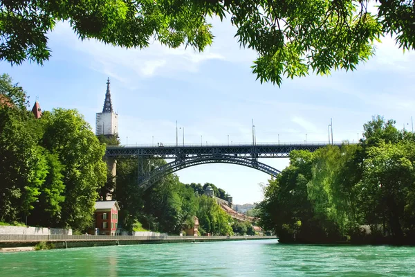 Beautiful panorama of the city of Bern and the emerald river Aare. Big bridge over the river. Summer urban landscape. Many white houses with red roofs. A lot of green trees. A good place to travel. Summer season. Switzerland.