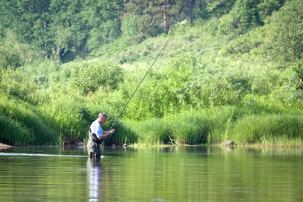 Summer fishing on the lake.  A man pulls a fish out of the river, in the hands of a fishing rod and net.  Beautiful summer landscape. A lot of green vegetation, reflected in the water. Summer season.