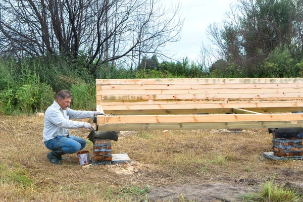Будівництво дерев'яного будинку в сільській місцевості. Дорослий чоловік малює будинок . — стокове фото