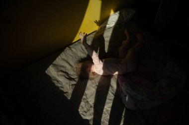 Sarı bir duvarda, güneşin altında oynayan bir kızın portresi.