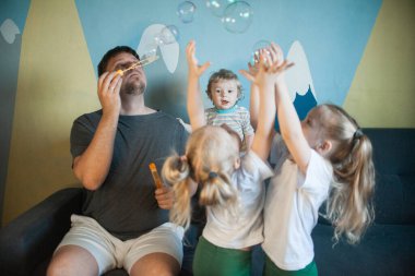  Babam evde çocuklarıyla sabun köpüğü oynuyor. Babam evde üç çocukla oynuyor: bir oğlan ve kızlar, erkek ve kız kardeşler.