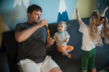  Babam evde çocuklarıyla sabun köpüğü oynuyor. Babam evde üç çocukla oynuyor: bir oğlan ve kızlar, erkek ve kız kardeşler.