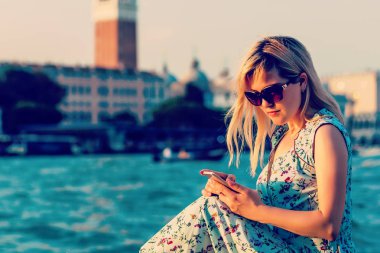 Güneş gözlüğü smartphone kullanarak canal yanında oturan kadın