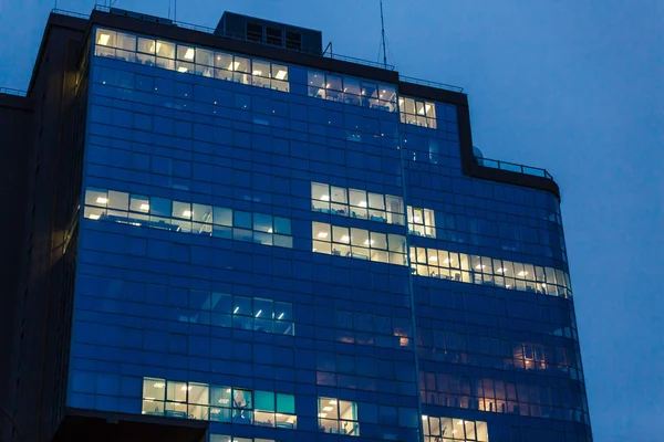 Windows of glass office building, lighting and working people within