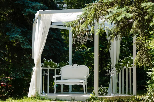 Beautiful wedding photo zone in green park in shade white bench, screen, pedestal with flowers and decor