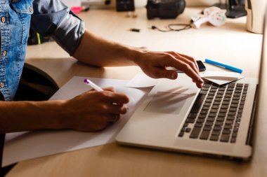 Akıllı telefon ve dizüstü bilgisayar kullanarak evden çalışan genç bir adamın kırpılmış atış silüeti 