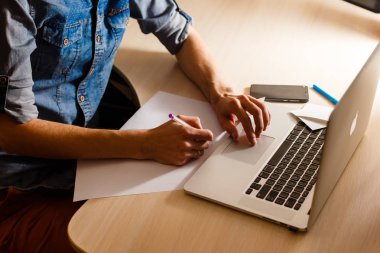 Erkeklerin ellerini bir tabletle dizüstü bilgisayarla kapatıp masada oturuyorlar.