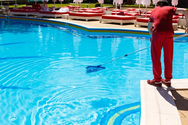 Bir fırça veya net yalınayak kenarında, düşük açılı görünümü alt vücudunun ıslak zeminde ayakta mavi kutup yazları yüzme havuzu temizlemeye adam.