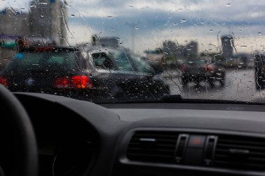 Ön cam, yağmurlu bir günde akşam, Araba ön cam görünümü, karanlık ve bulanık arka plan üzerinde şehir trafiğinde üzerinde su damlaları.