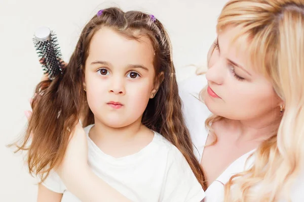 年轻的母亲刷头发的小女儿在一个白色的背景 妈妈梳理女儿 — 图库照片