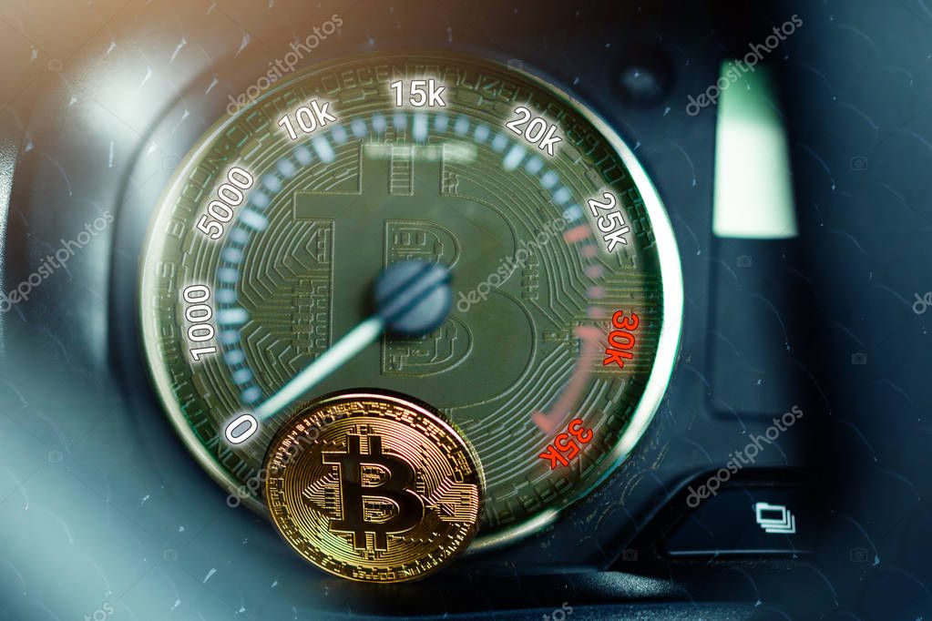 The physical coin is a gold bitcoin on the dashboard of the car next to the fuel consumption