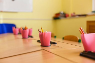 Bir cam, ahşap bir masa ve okul için renkli kalemler.