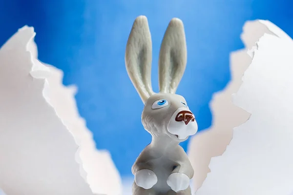 Little white toy rabbit sitting on a big white egg on a blue background