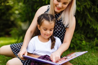 Oldukça genç anne ve küçük kızı yeşil çayır üzerinde oturan photobook arıyorsunuz