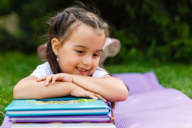 Küçük bir kız çimlere okuma onun karnına yatıyor. O yüzündeki keyfi bir görünüme sahip ve çok rahat görünüyor. Onun etrafında negatif boşluk biraz.