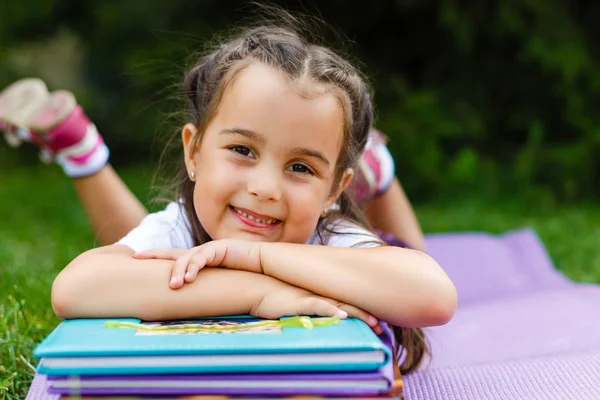 küçük kız parkta bir kitapla çim üzerinde yalan