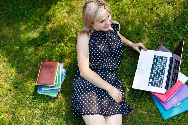 stock image beautiful young student girl smiling lying on green grass with opened laptop and books