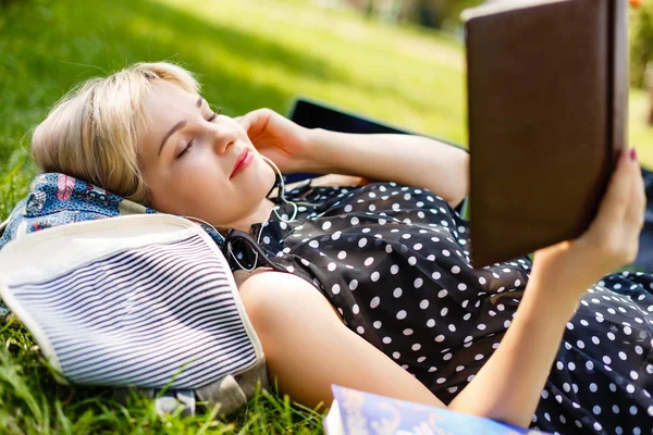 Woman lay down or relaxing on green grass reading book in summer or spring, top view