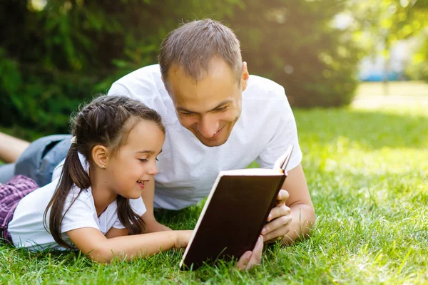 yeşil çim üzerinde yalan onun küçük kızı okuma kitabı ile genç baba