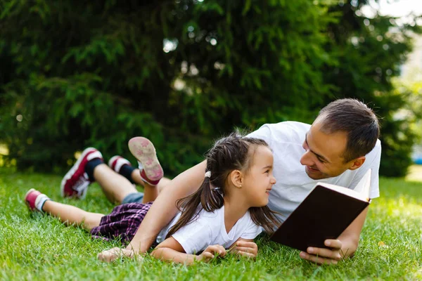 Молодий Батько Своєю Маленькою Донькою Читає Книгу Лежить Зеленій Траві — стокове фото