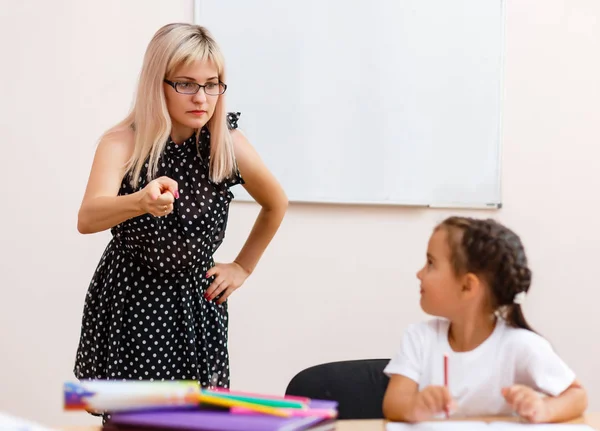 strict teacher and a little student. Little girl is crying at a desk in the classroom