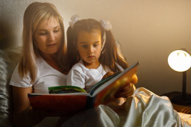 yatağa yatmadan önce kitap Genç Anne ve küçük kız okuma