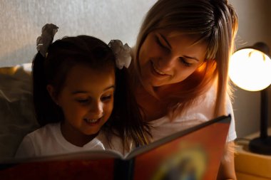 yatağa yatmadan önce kitap Genç Anne ve küçük kız okuma