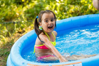 Little girl in an inflatable pool in the garden near the house clipart