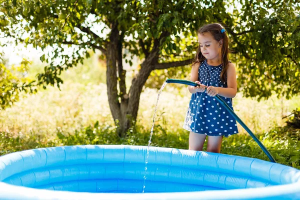 Little girl pours water into the inflatable children\'s pool