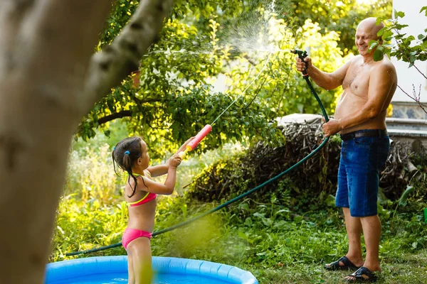 祖父と孫娘は 家の近くの庭で膨脹可能なプールの水でお互いを注ぐ — ストック写真