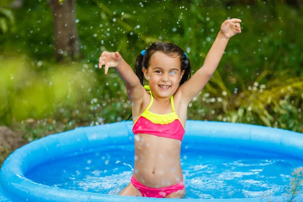 Little girl in an inflatable pool in the garden near the house