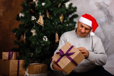 hediye kutusu ile Noel ağacının yanında oturan dede