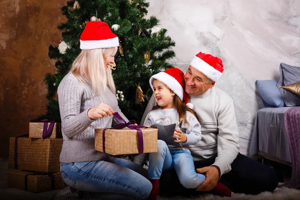 母と祖父の家でのクリスマス ツリーが座っているギフト ボックスを開く少女 — ストック写真