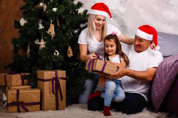 Noel ağacı yakınındaki kızı ve torunu ile vakit Santa şapkalı yaşlı adam