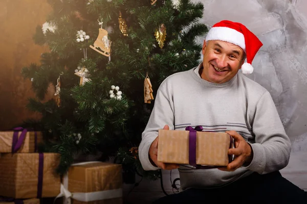 ギフト用の箱のクリスマス ツリーのそばに座っての祖父 — ストック写真