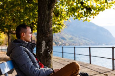 Genç adam parkta bankta oturuyor.