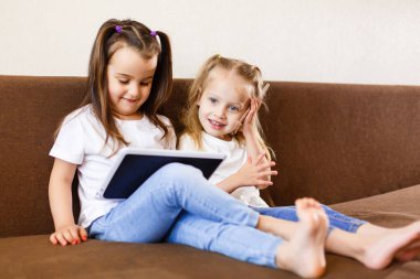 Dokunmatik yüzey ve smartphone kullanarak ve evde koltukta oturan iki küçük kız