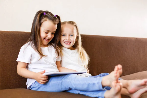 Duas Irmãs Adoráveis Brincando Com Tablet Digital Sentado Sofá Casa — Fotografia de Stock