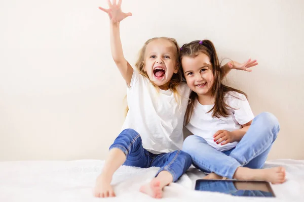 Twee Gelukkige Kleine Meisjes Knuffelen Zittend Bed Met Digitale Tablet — Stockfoto