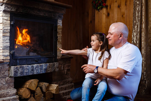 Grandfather and granddaughter spending time near fireplace
