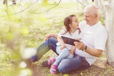 Torunu sarılma ve dijital tablet parkta oturan kullanma Büyükbaba.