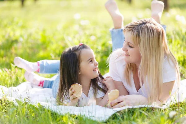 Happy mom and daughter spending time in green park and eating ice-cream