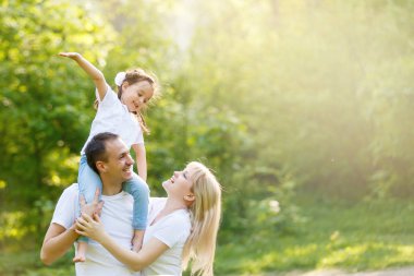 Üç birlikte eğleniyor genç mutlu aile açık. Küçük kızı baba sırtında. Anne ve kız mutlu bak ve gülümse. Mutluluk ve uyum içinde aile hayatı. Aile eğlencesi dışında.
