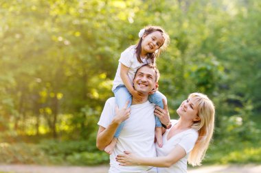 Üç birlikte eğleniyor genç mutlu aile açık. Küçük kızı baba sırtında. Kızı sırtlama taşıyan ve gerçekten mutlu baba