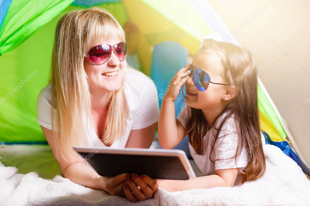  Young mother and her daughter wearing sunglasses having fun with tablet
