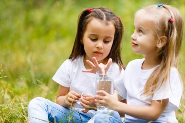 Two little girls drinking glass of water in green park. Concept of purity, ecological and biological product, love for nature clipart