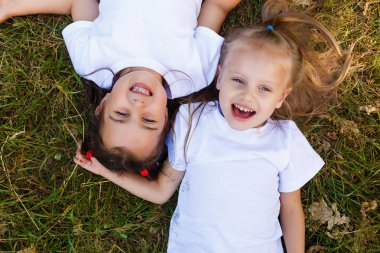 Two little smiling girls lying on the grass in the park clipart