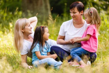 İki anne ve iki küçük kızı eğleniyor yeşil Park'ta dinlenme 