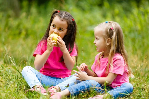 Дві Маленькі Дівчата Їдять Яблуко Сидячи Парку Зеленій Траві — стокове фото