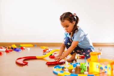 Kapalı yerde çok sayıda renkli plastik basamak veya sayı ile oynayan küçük kız çocuk.
